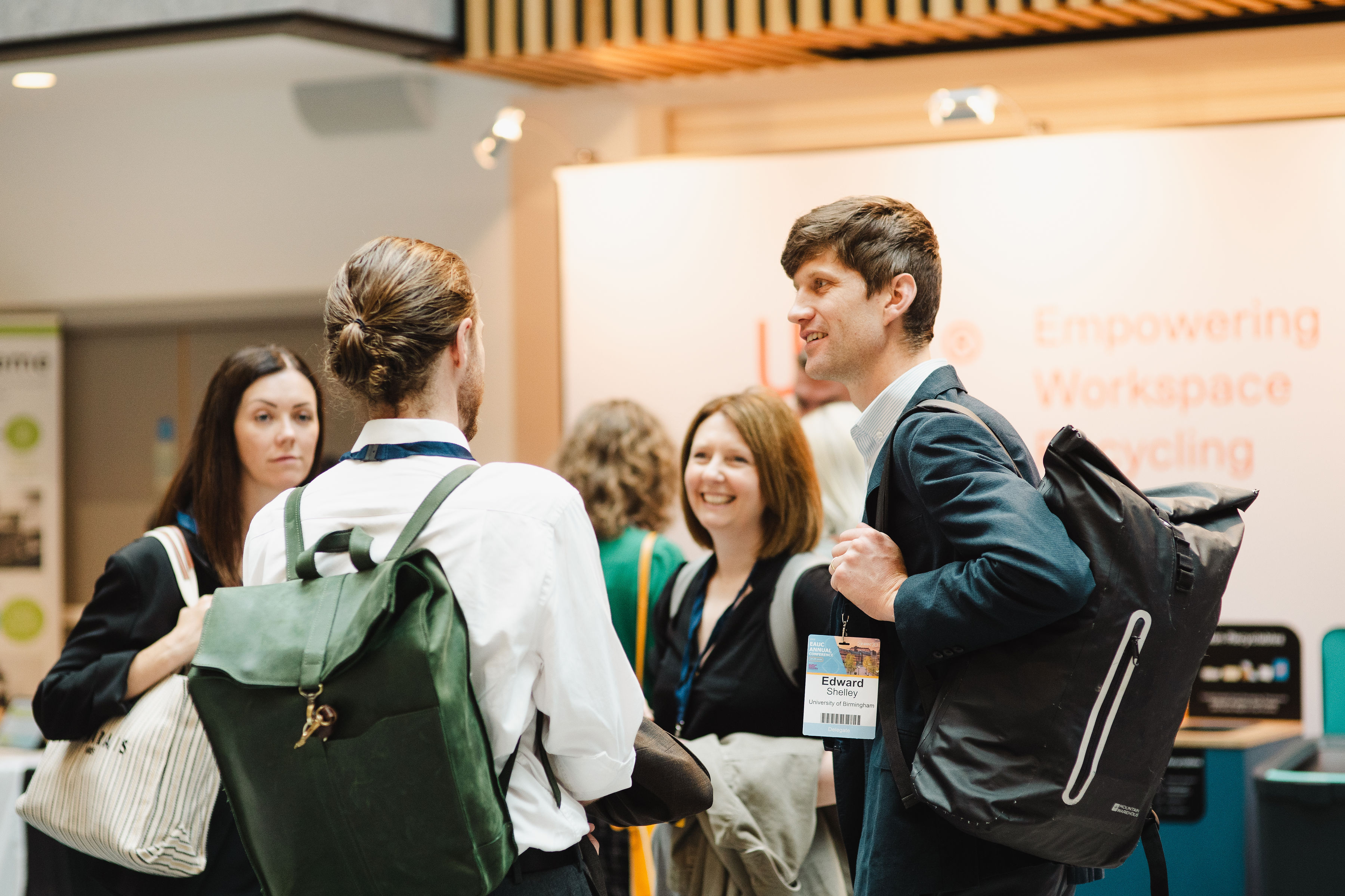 A man with a rucksack and his back to the camera speaks to another man with a rucksack and two women facing the camera