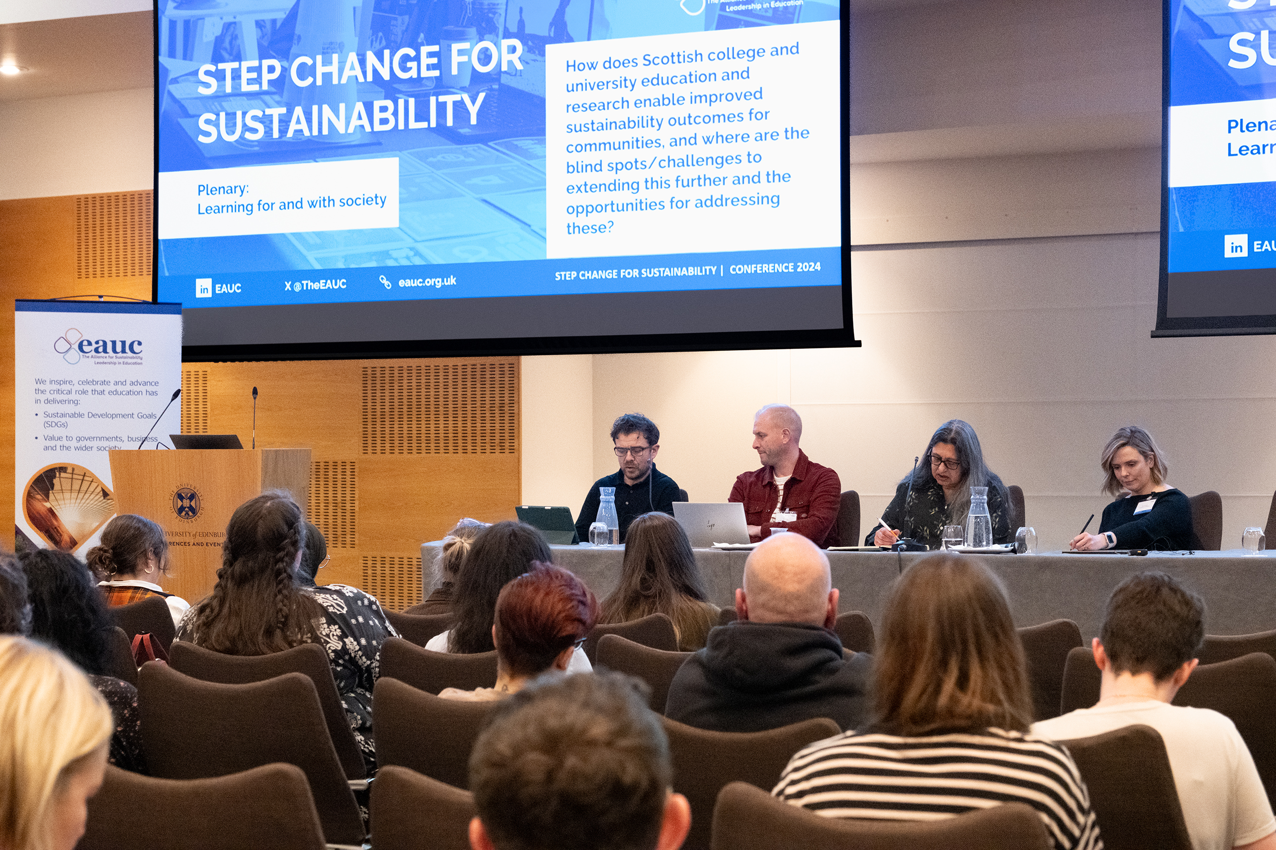 A panel of speakers beneath a screen reading "Step Change for Sustainability"