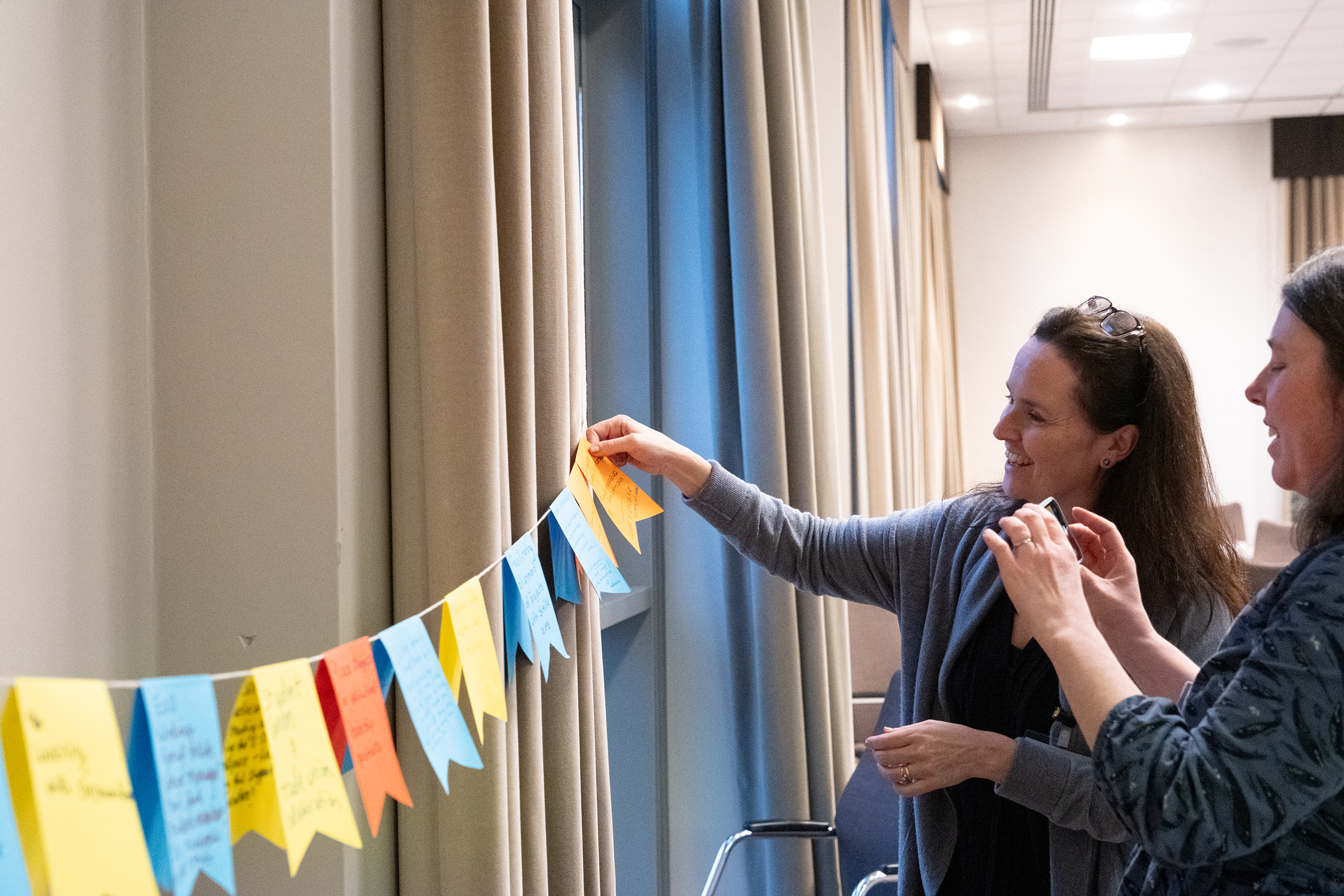 Two people hanging bunting made up of post-it notes. 