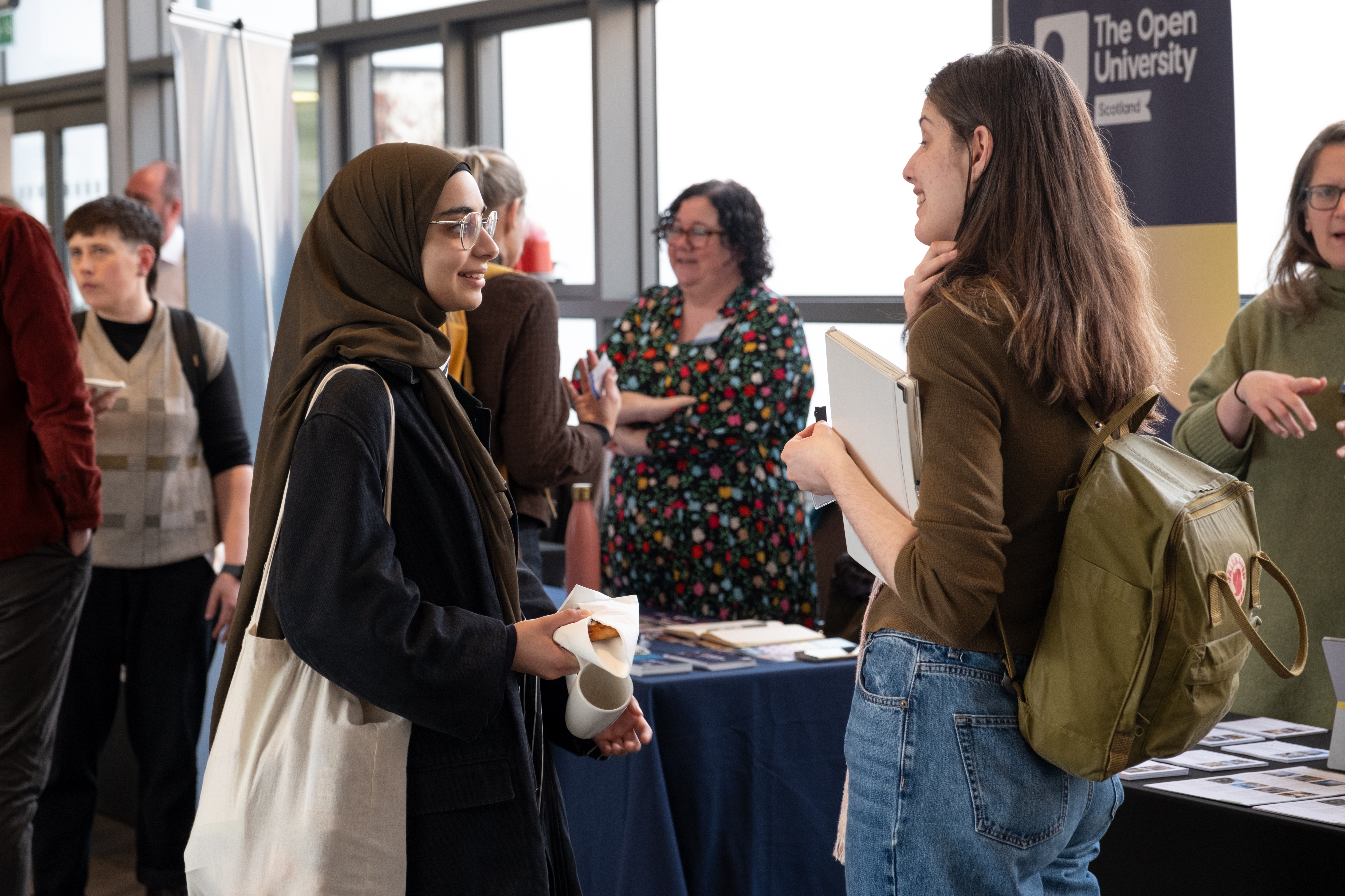 Two people chat to each other at a conference with delegates in the background 